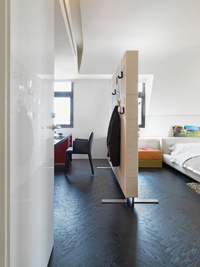 Blick durch offene Tür in ein Appartement mit Raumteiler zwischen Schlaf- und Arbeitsbereich