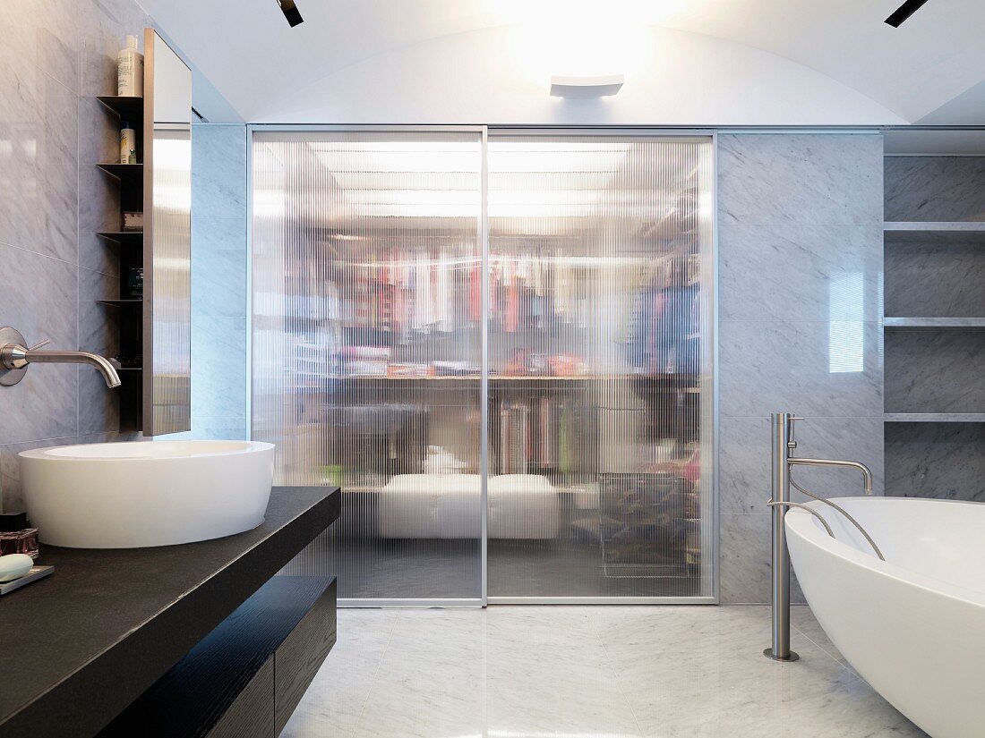 Modern washstand and free-standing bathtub in front of integrated dressing room with closed sliding glass doors