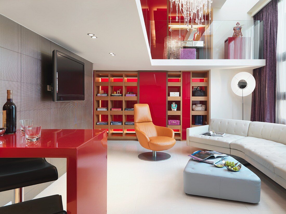 Farbakzente und Designermöbel vor hinterleuchtetem Einbauregal im Wohnraum mit Galerie