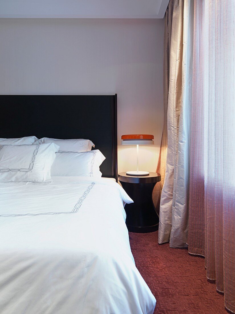 Doppelbett mit weisser Bettwäsche neben Nachttisch mit Leuchte im Retrostil