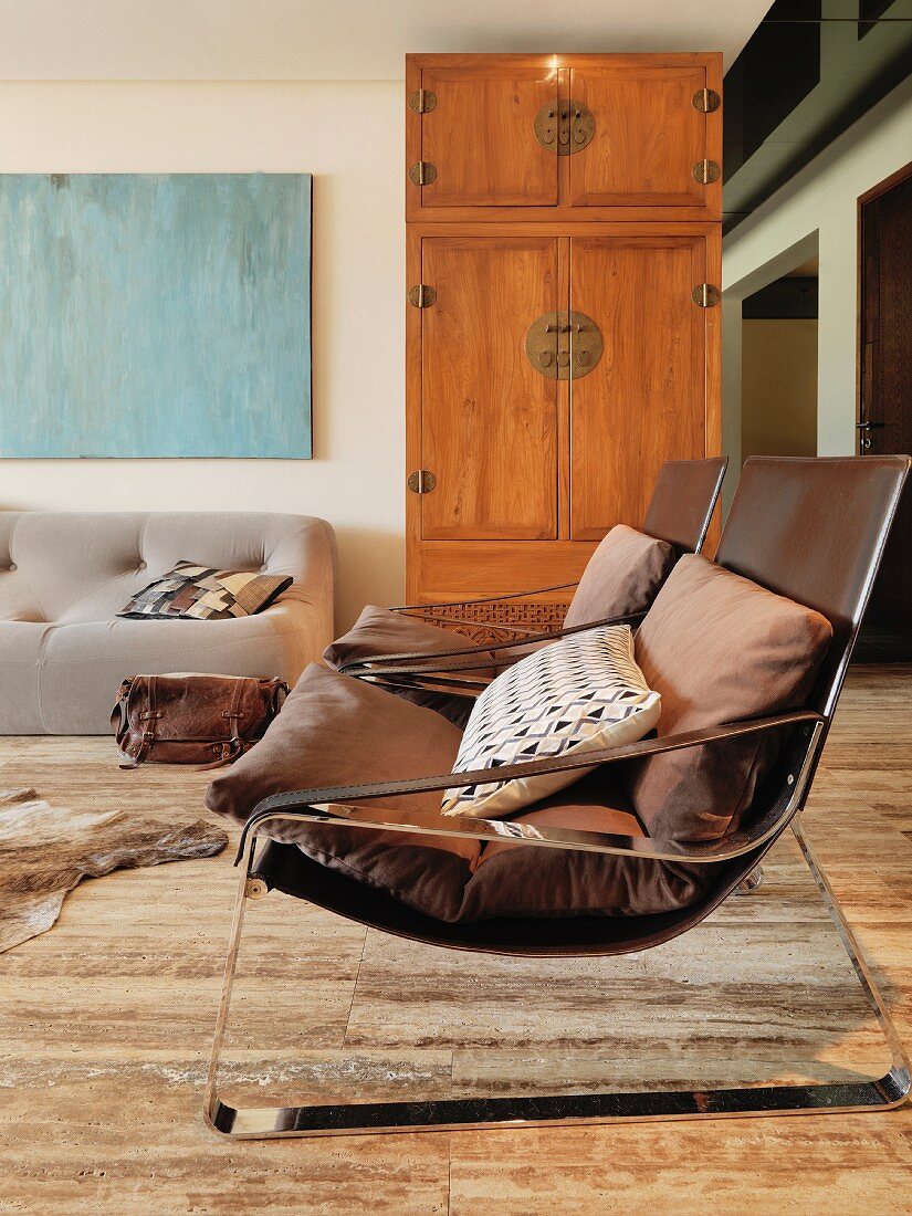 Sessel mit Lederbezug und Kissen vor schlichtem Holzschrank in asiatischem Stil
