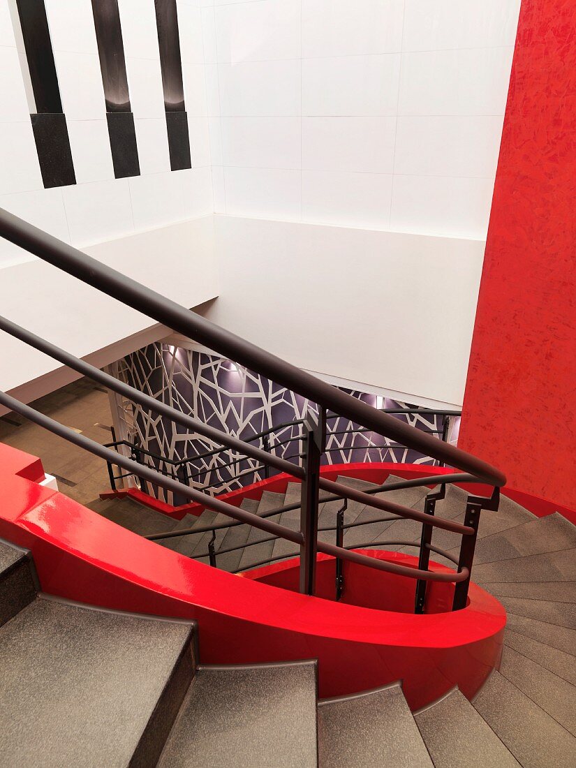 Schneckenförmiges Treppenhaus mit roter Innenwange und schwarz lackiertem Treppengeländer