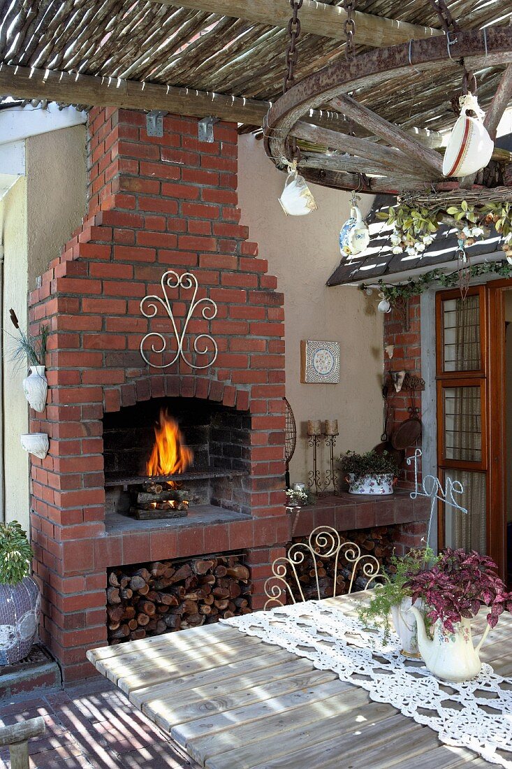 View across wooden table of fire in brick outdoor fireplace on veranda