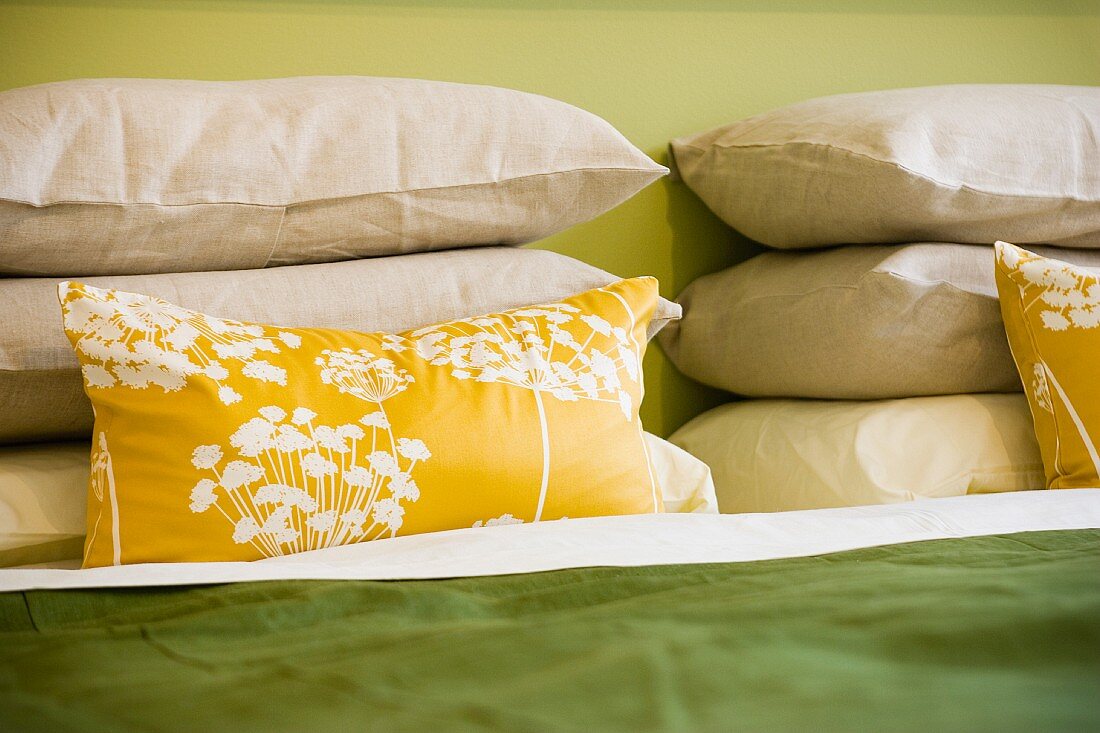 Gelbes Kissen mit modernem Blumenmuster vor Kissenstapel auf Bett