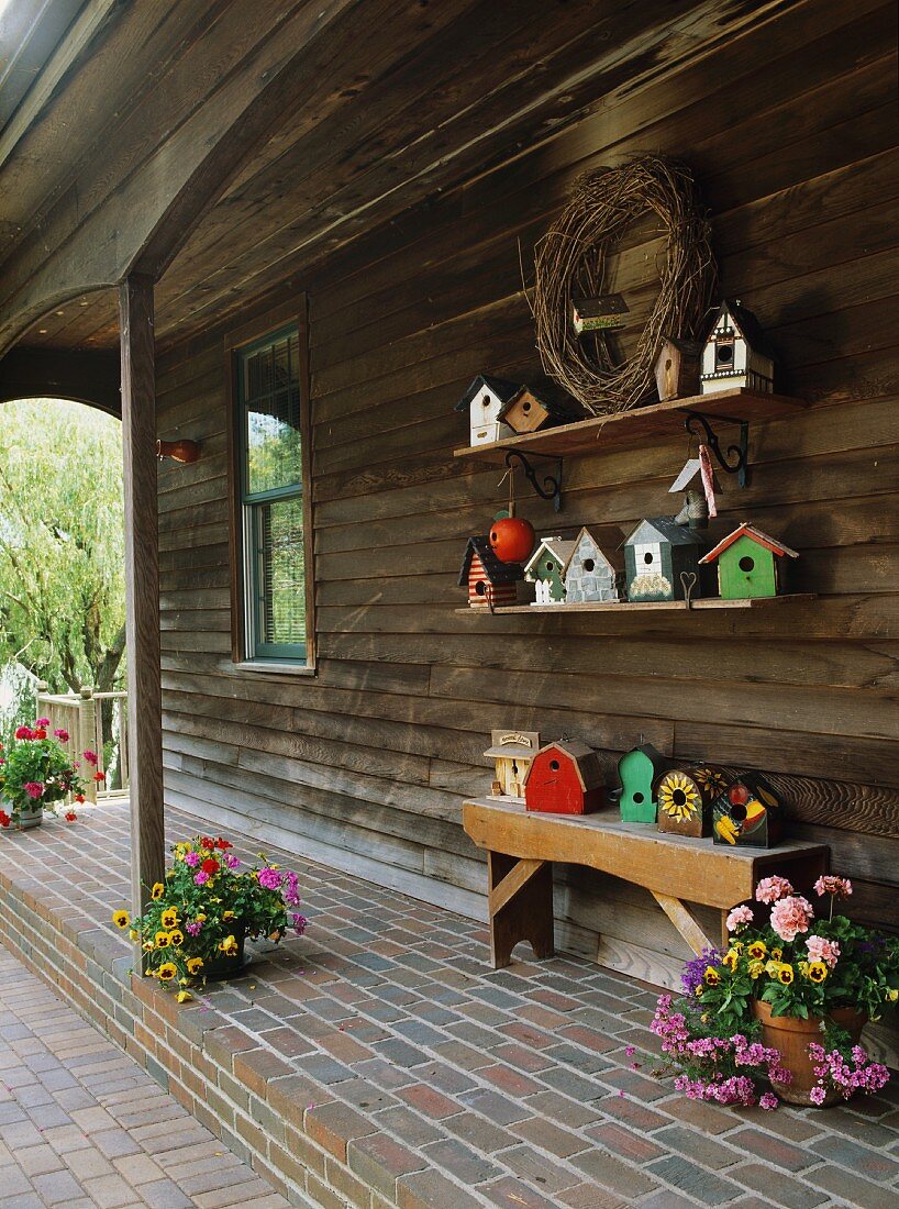 Holzhaus mit überdachter Veranda, mit Sitzbank, Blumendeko und einer Vogelhäuschensammlung