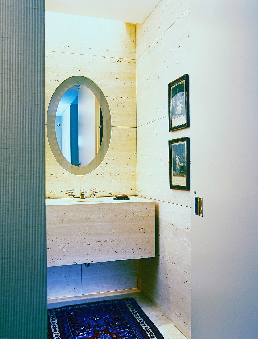 Badezimmer mit Steinfliesen an der Wand, einem Steinwaschtisch und einem ovalen Spiegel