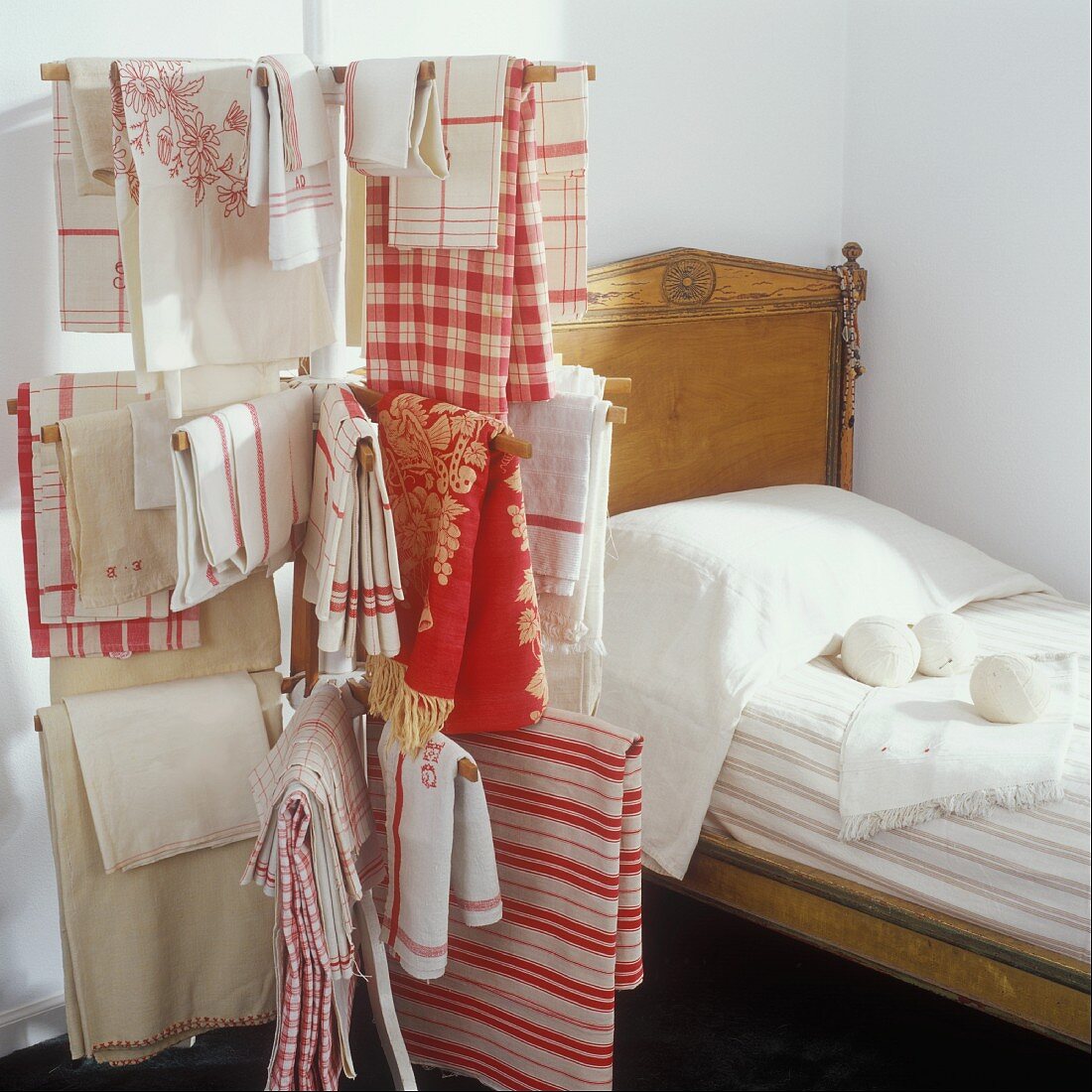 Antikes Bett mit an einem Wäschetrockner hängender Vintage-Wäsche in Rot-Weiß