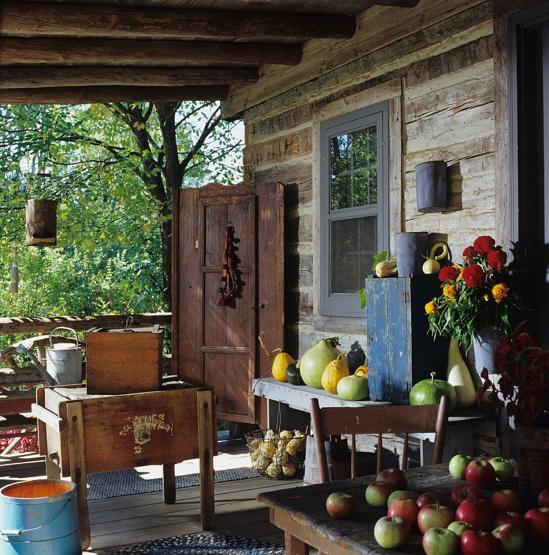 A rustic veranda outside a wooden cabin with freshly picked garden fruits and a bunch of summer flowers
