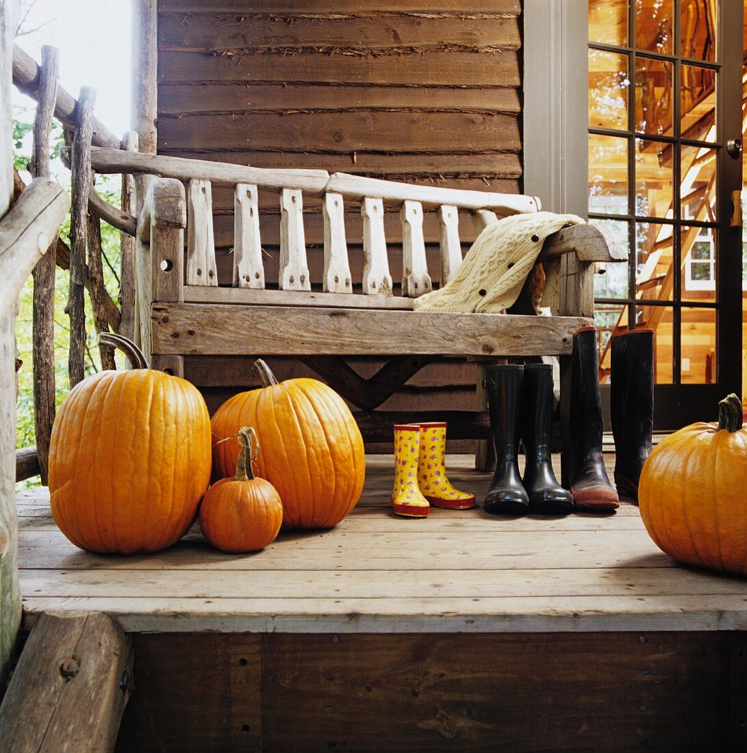 Old wooden bench on veranda behind large pumpkins and wellingtons