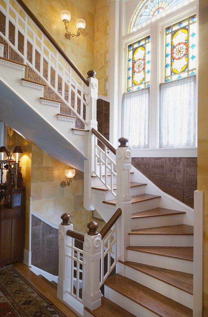 Feudaler Treppenaufgang mit kunstvollem und buntem Bleiglasfenster und mit geschnitzer Holzverkleidung an der Wand