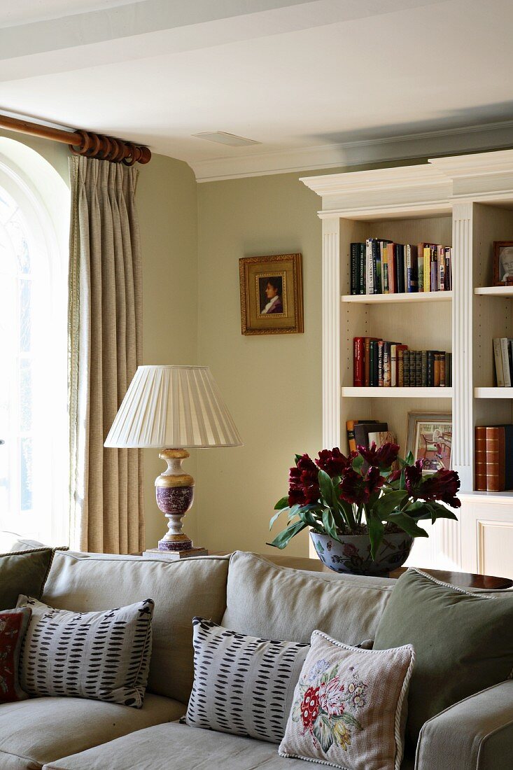 Traditional living room with grey upholstered sofa in front of white-painted, antique-style shelving