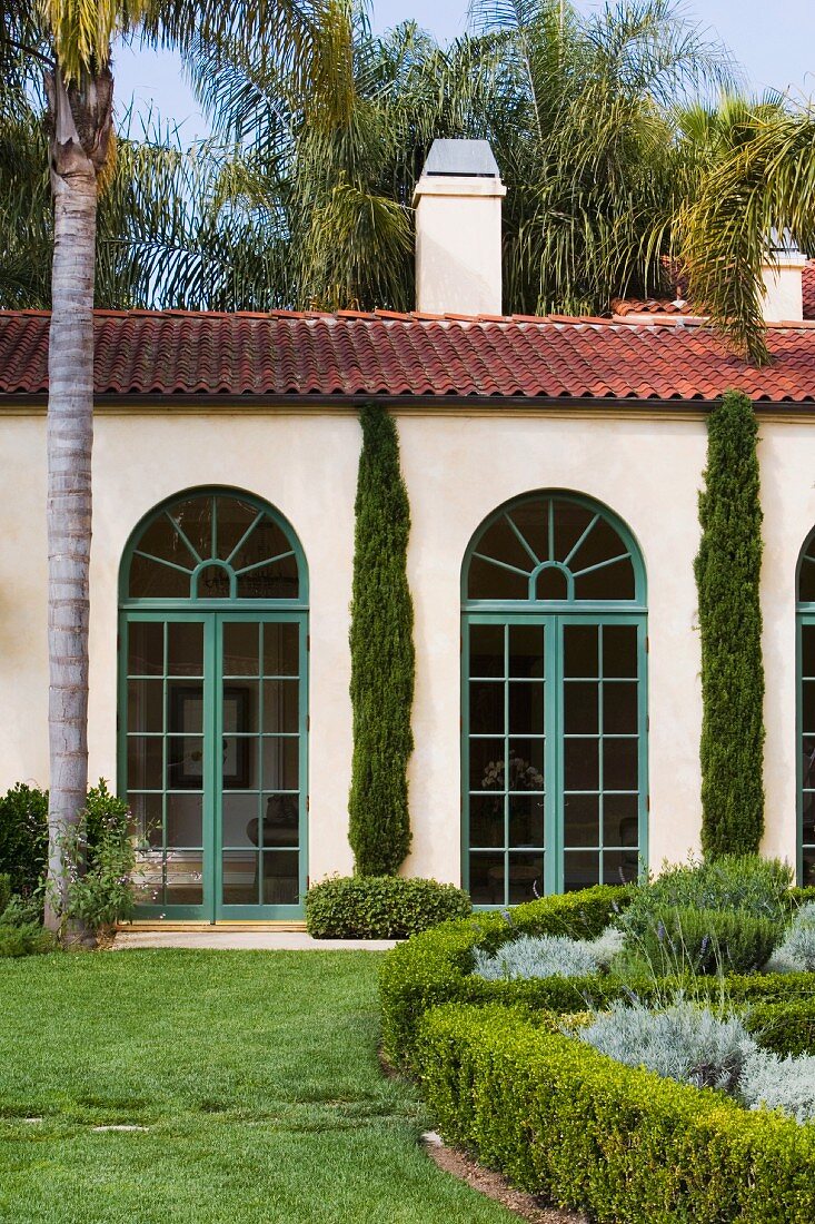 Gepflegter Garten mit Palmen vor Haus mit Rundbogenfenstern