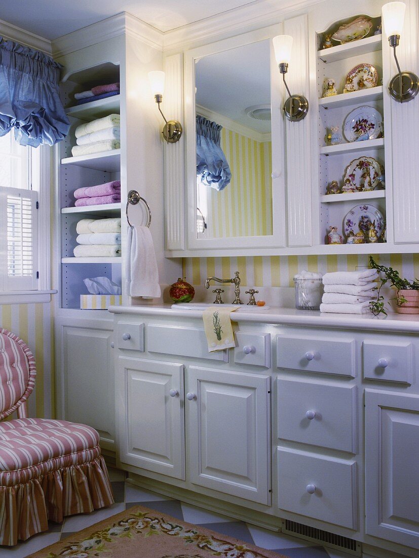 Nostalgisches Badezimmer mit weissen Einbaumöbeln, integriertem Badezimmerspiegel, ein Regal mit chinesischem Porzellan und einem langen Waschtisch