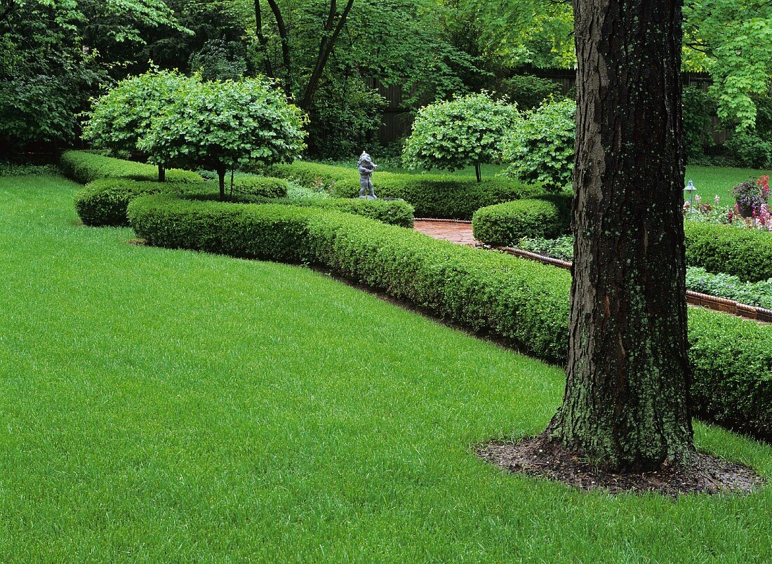 Park mit gepflegter Wiese, einem von Hecken gesäumten Gartenweg und einer zentralen Skulptur