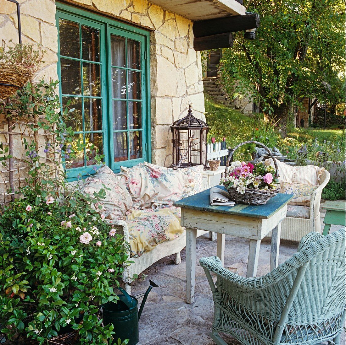 Gartenterrasse eines Natursteinhauses mit Vintage-Möbeln und einem dekorativen Blumengesteck in einem Korb