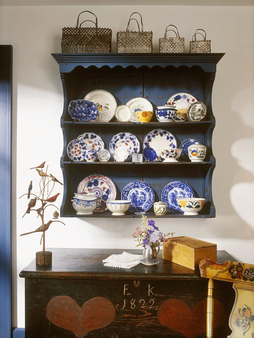 Rustic crockery shelf with collection of plates and pots, collection of baskets on top and antique wooden trunk painted with date and hearts