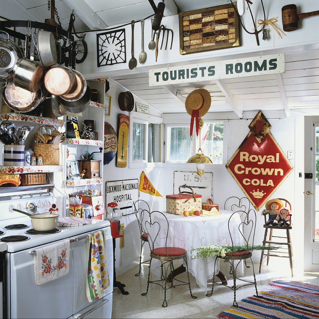 Kitchenette with corner window, round dining table, delicate metal chairs, old-fashioned cooker and colourful collection of signs