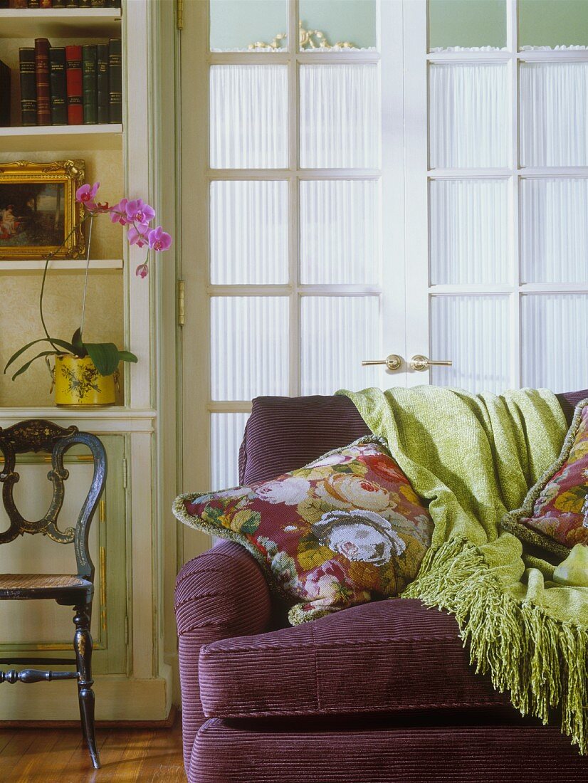 Corduroy sofa with floral cushions and fringed throw: screened French windows in background