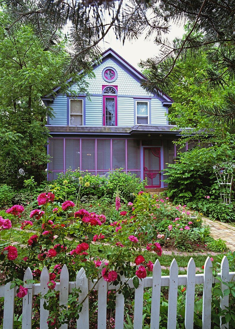 Idyllisches, hellblaues Holzhaus mit verglaster Veranda und einem schönen Blumengarten mit weißem Holzzaun