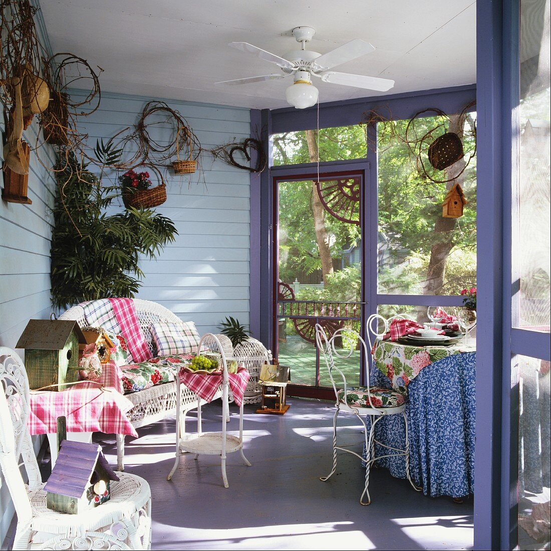 Verglaste Veranda mit Korbmöbeln und einem Deckenventilator; gemusterte Textilien sorgen für ein heiteres Ambiente