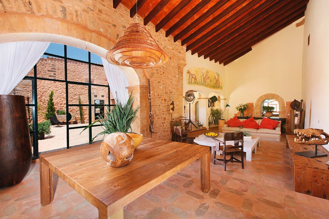 Holztisch in offenem Wohnraum eines mediterranen Landhauses und Blick in Innenhof