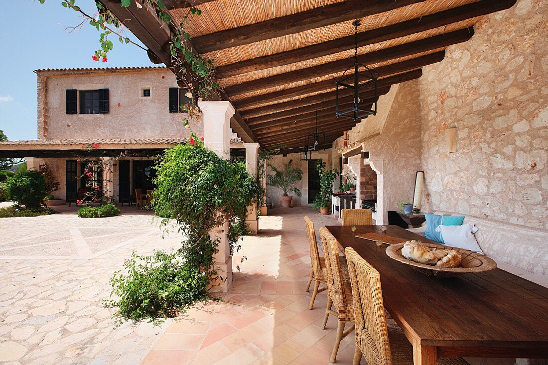 Holztisch und Stühle unter Vordach eines mediterranen Landhauses mit Innenhof