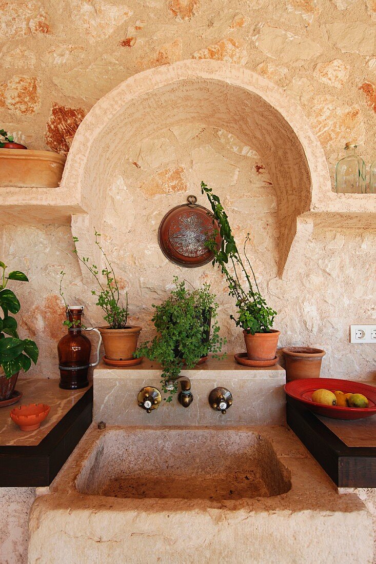 Ausschnitt einer rustikalen Küche mit gemauertem Küchenbecken vor Natursteinwand