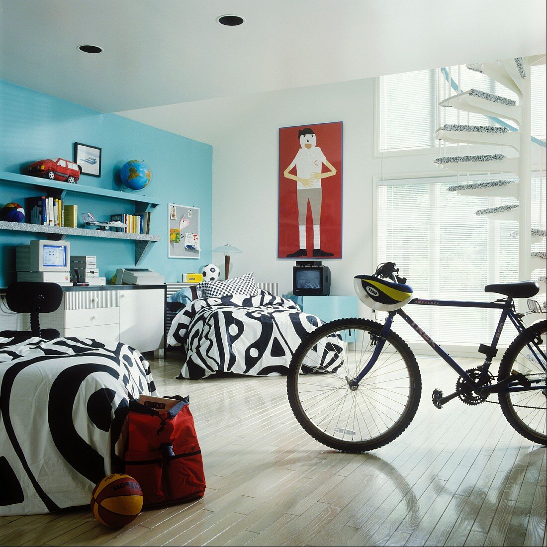 Boys' room with blue wall, black and white bedspreads, desk and bike