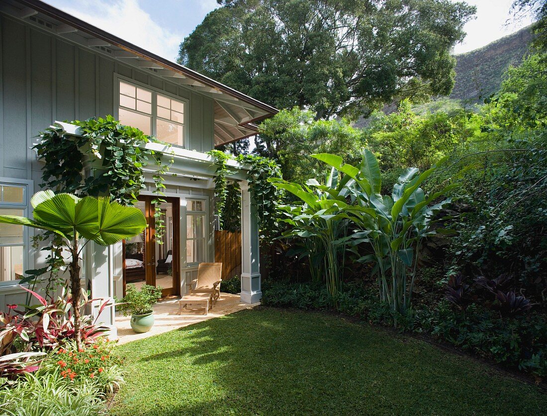 Überdachte Terrasse einer eleganten Landhausvilla mit Bananenstauden im Garten