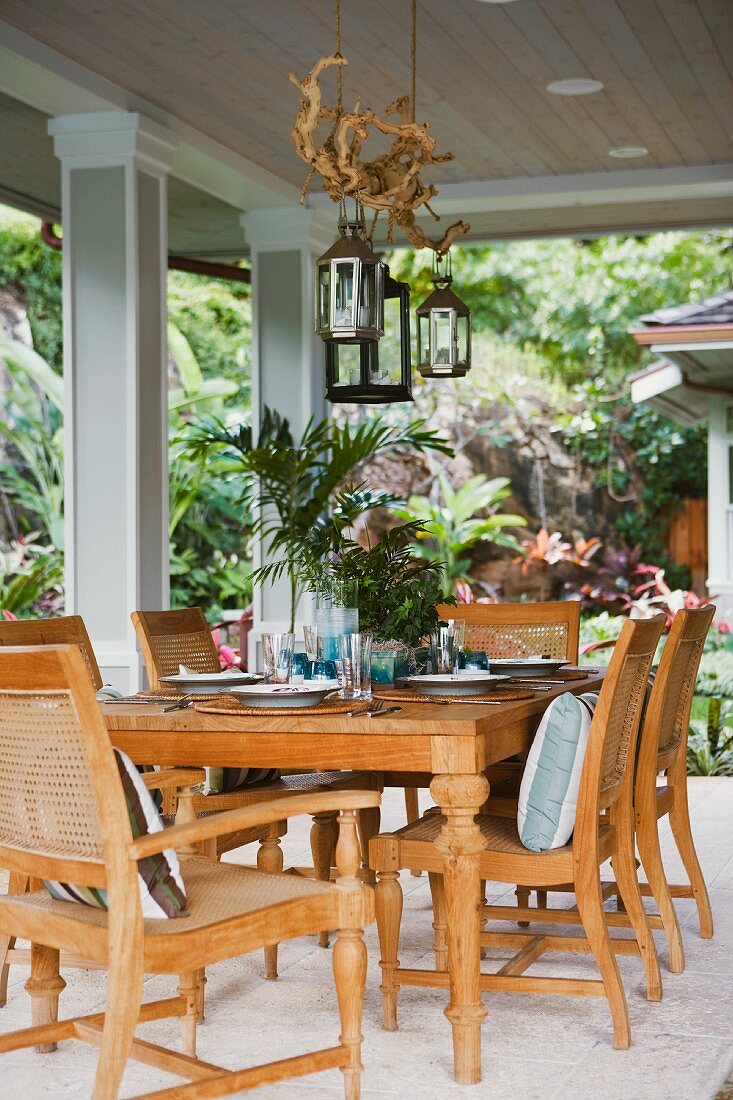 Gedeckter Tisch mit hellen Landhausmöbeln auf überdachter Holzveranda