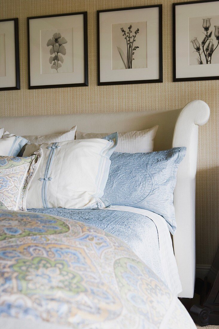 Gerahmte Pflanzenfotos über dem gepolsterten Kopfteil eines Doppelbetts mit Sammlung passender Kissen und Decken