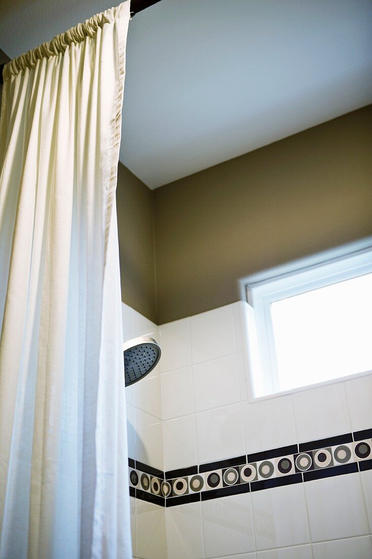 Blick durch den geöffneten Duschvorhang auf Fliesenbordüre mit schwarz/grauem Kreismuster