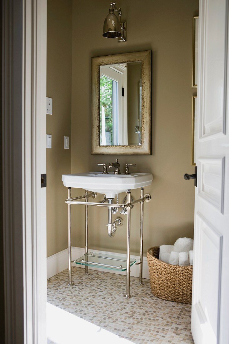Blick durch die offene Tür auf Waschbecken mit verchromtem Stahlgestell vor beigebraun getönter Wand