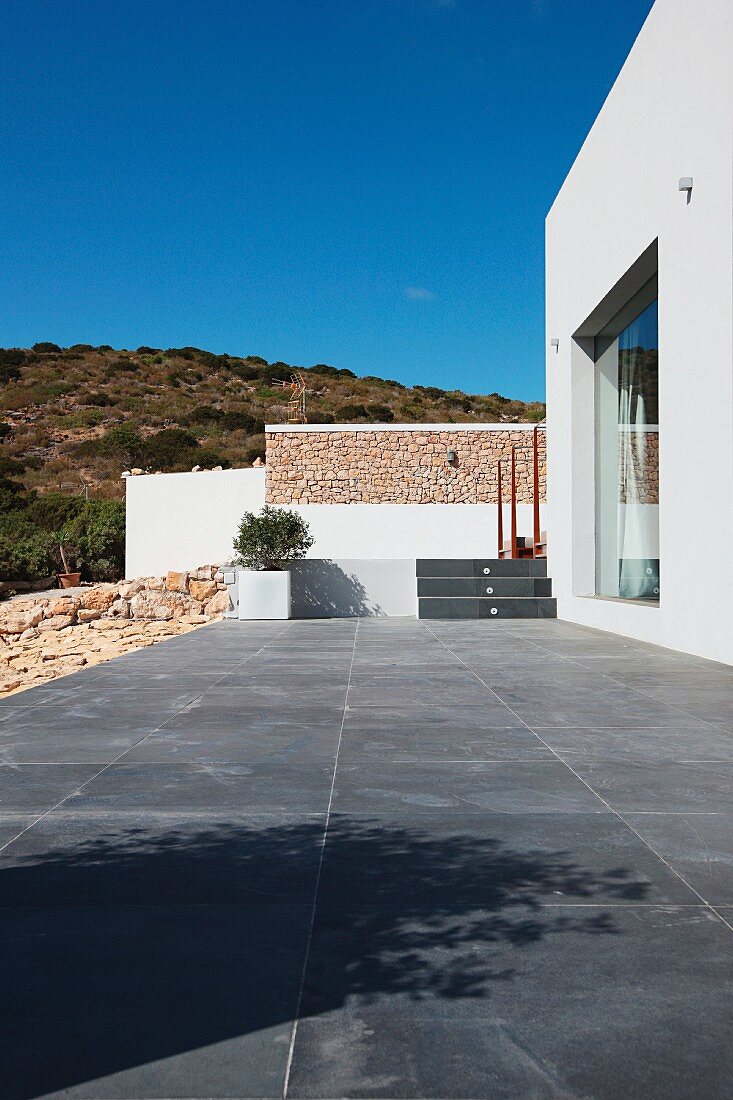 Terrasse mit grauen Fliesen vor zeitgenössischem Wohnhaus in mediterraner Lage