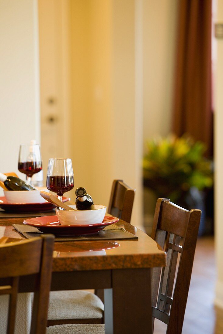 Ecke eines gedeckten Tisches mit gefülltem Weinglas und kleiner Weinflasche in Suppenschüssel