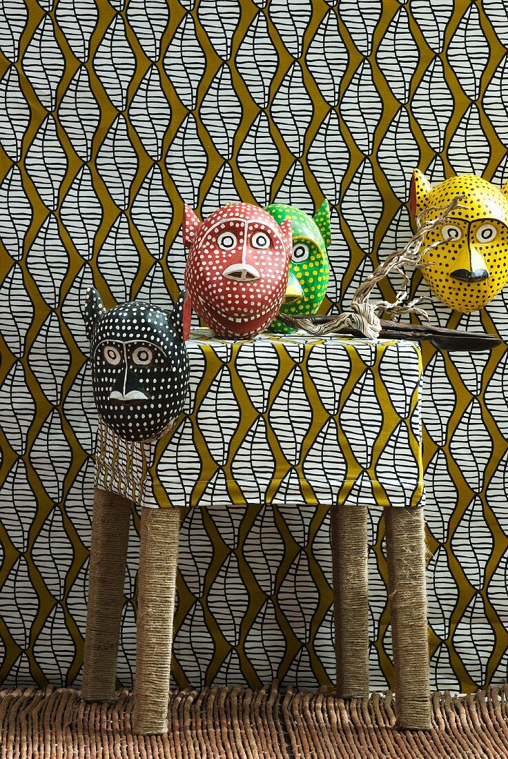 Colourful animal masks on stool and on wall covered in patterned fabric