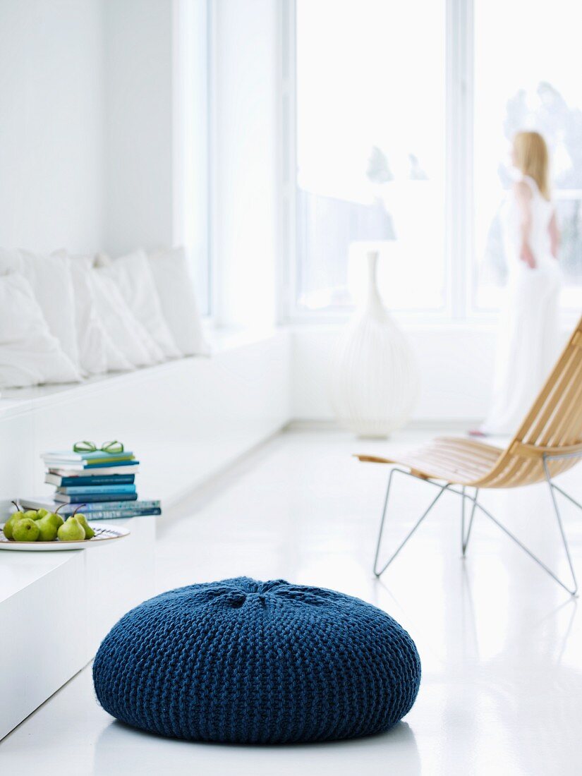 Floor cushion with hand-knitted, blue cover in minimalist, white interior