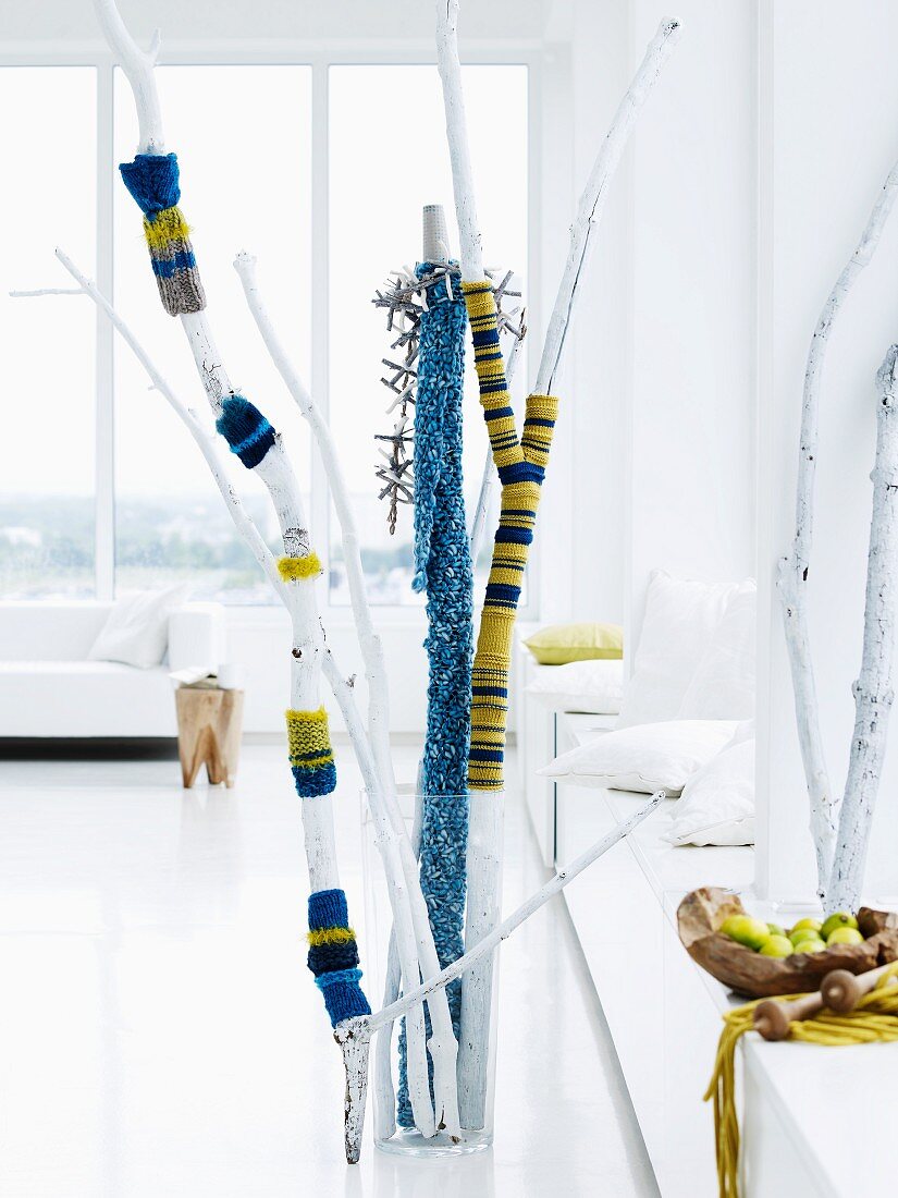 Branches covered with blue and yellow striped, knitted textiles as decoration in reserved, white interior