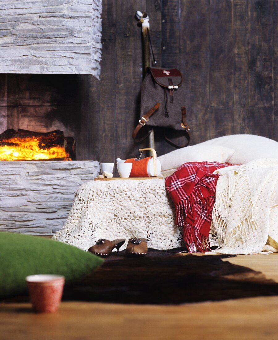 Häkeldecke und Wolldecken auf einem Bett neben dem Kamin