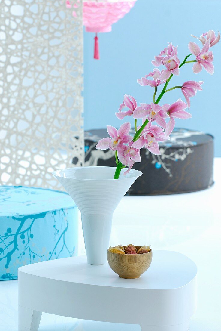 Weißer Beistelltisch mit rosafarbener Orchidee in weißer Vase, dahinter japanische Sitzkissen vor hellblauer Wand