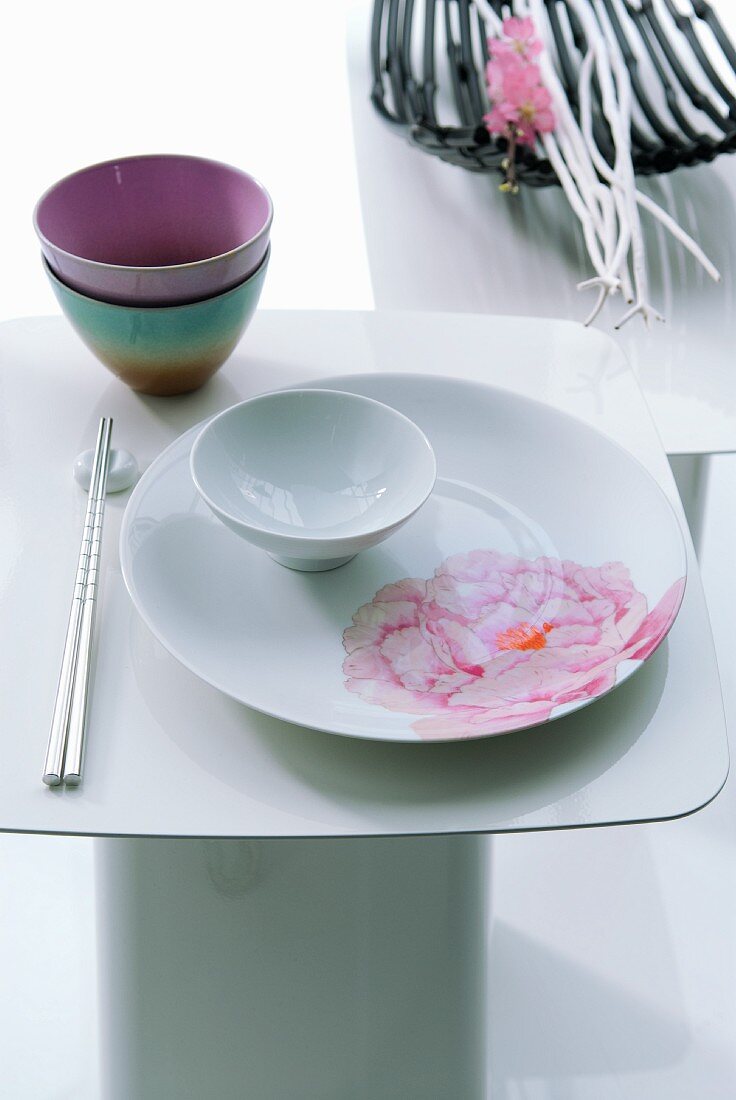 Japanisches Tischgedeck auf weißem Beistelltisch im Hintergrund Dekoschale mit Ästen und Blütenzweig