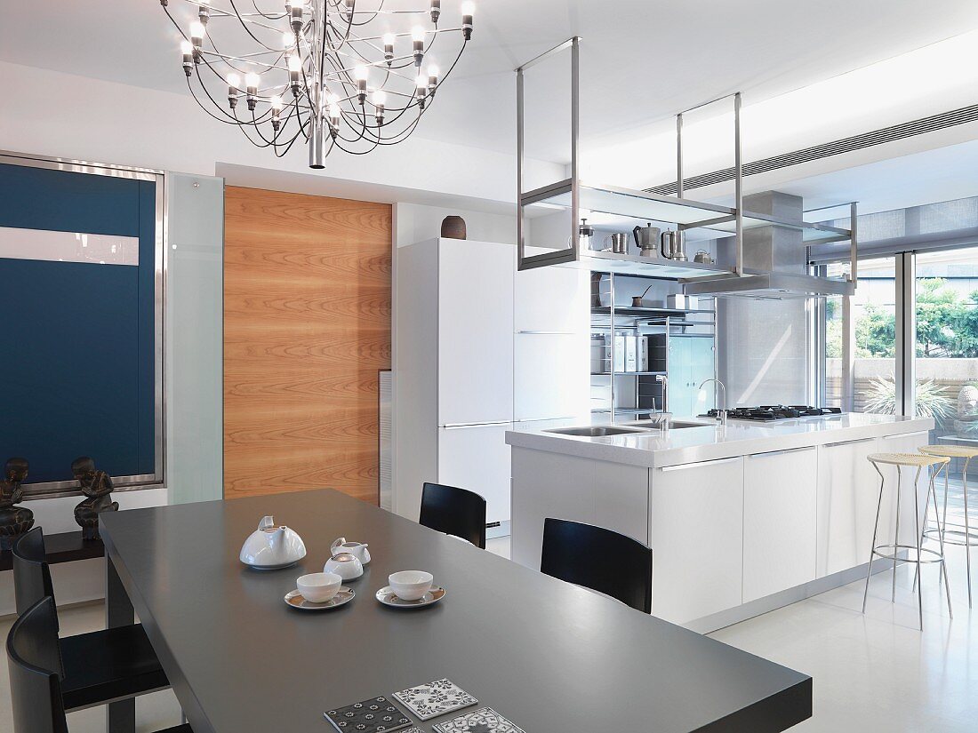 Grauer Esstisch unter Designer Hängelampe vor offener Küche mit freistehendem Küchenblock in Weiß