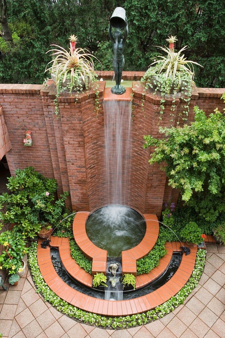 Arrangement of fountains and waterfall against high brick wall in courtyard