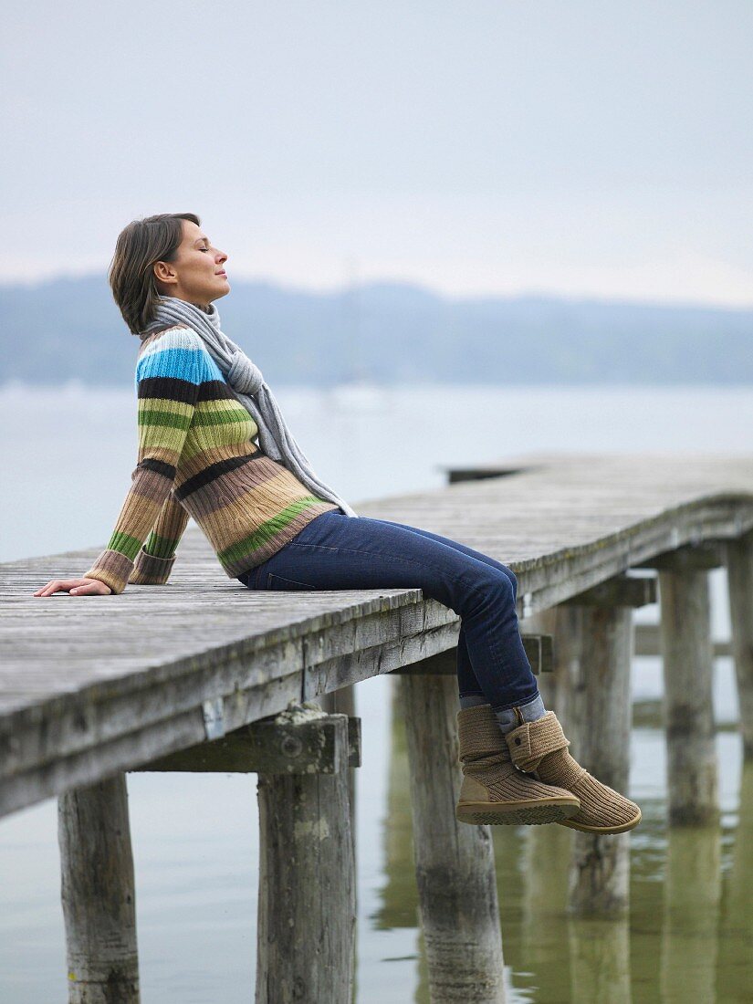 Frau sitzt auf einem Holzsteg am See