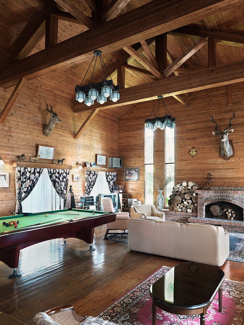 Großes Wohnzimmer in einem Holzhaus, mit offenem Kamin aus Ziegelsteinen und einem großen Billardtisch