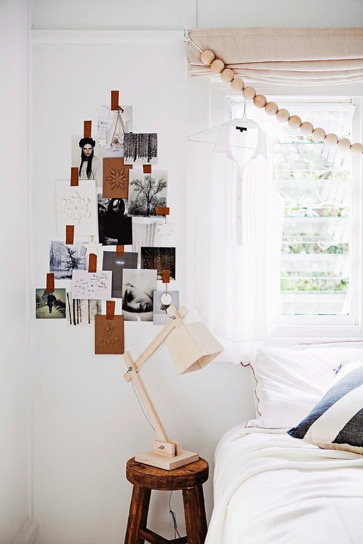 Holzkugelgirlande vor dem Fenster, Fotos in Tannenbaumform arrangiert an der Wand und Klassiker Schreibtischleuchte aus Holz neben Bett