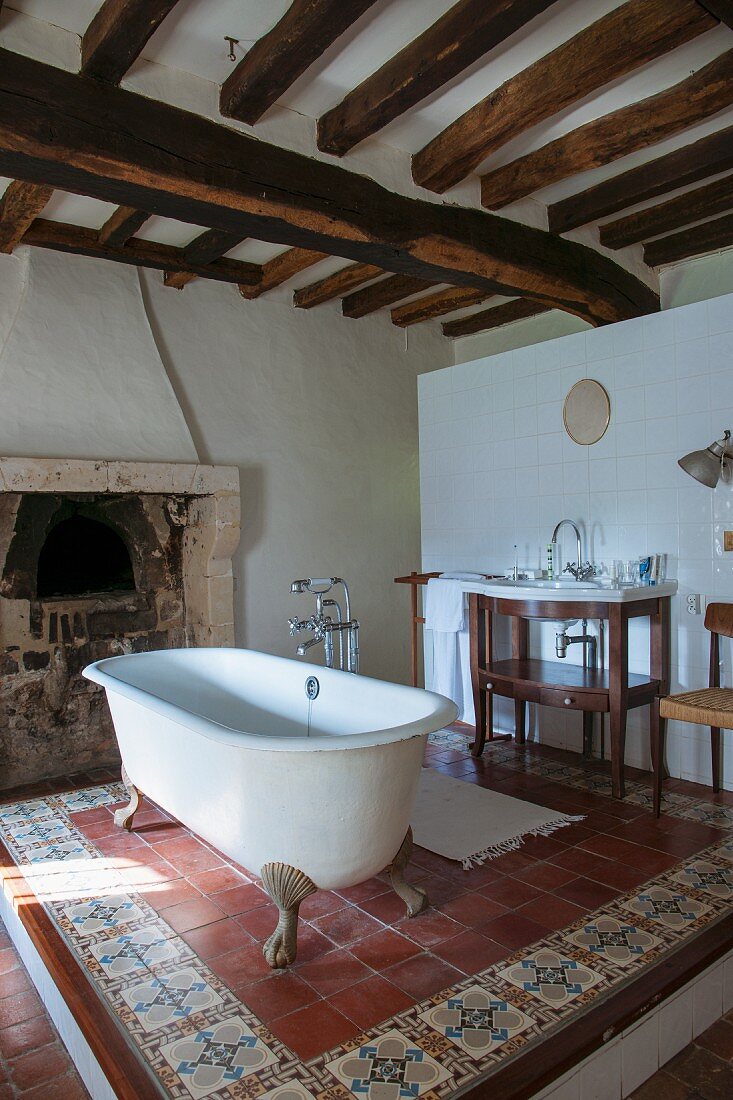 Free-standing bathtub on tiled platform below rustic wood-beamed ceiling