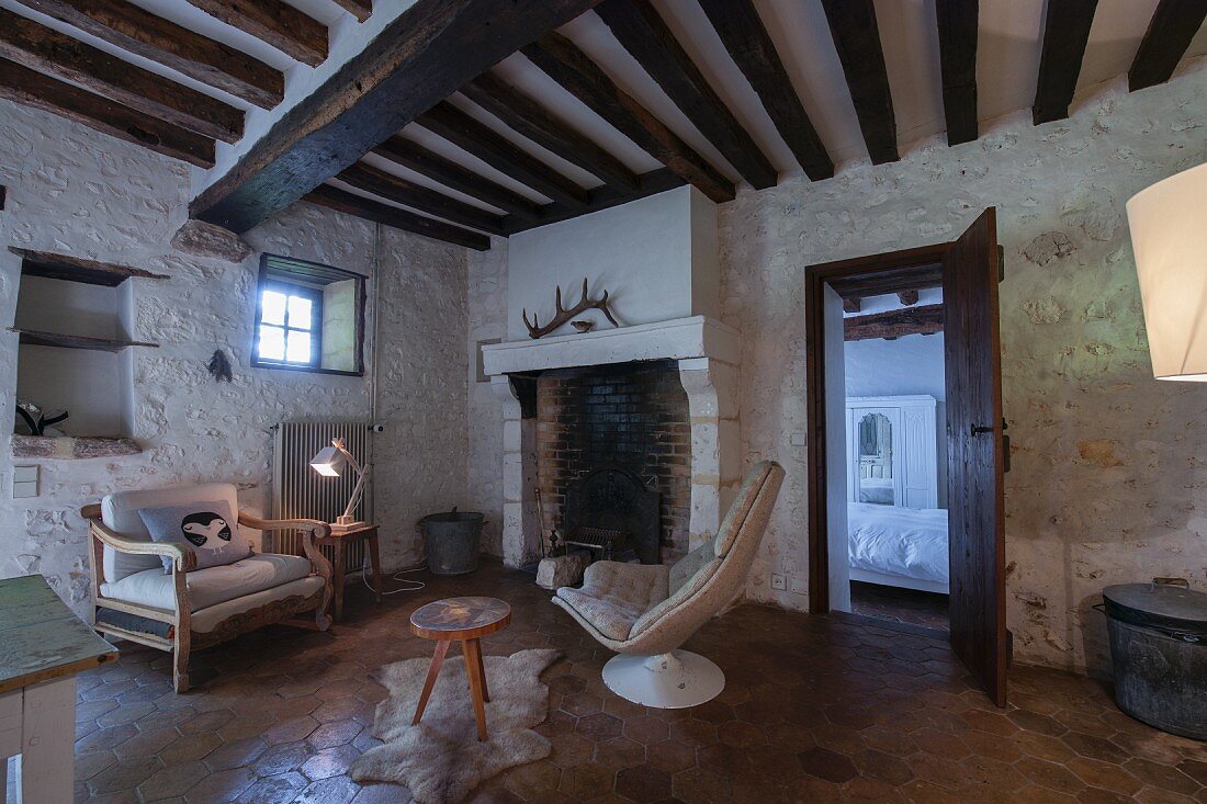 Fireplace in living room with tiles floor, whitewashed stone walls and rustic wood-beamed ceiling