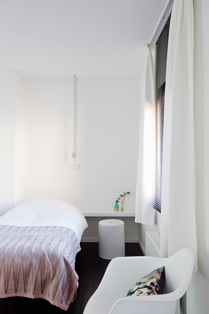 Kleines, minimalistisches Zimmer mit Einzelbett, im Vordergrund Klassikerstuhl in Weiß