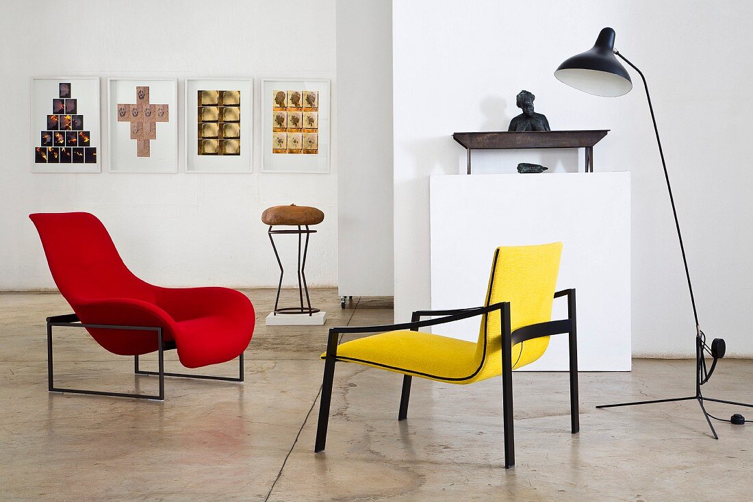Colourful, designer easy chairs and retro lamp surrounded by artworks in interior with polished concrete floor